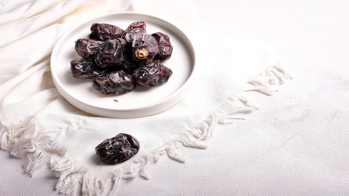 A white plate filled with premium dark ajwa dates displayed on a fringed cloth.